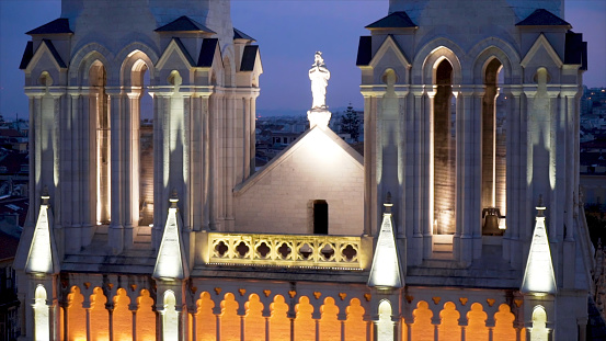 Sculpture of praying woman at Cathedra. Action. Illuminated statue of praying woman is located on roof of cathedral above city in evening.