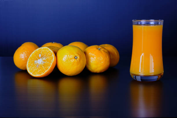 стакан апельсинового сока и группа свежих апельсинов на черном фоне. - orange black horizontal saturated color стоковые фото и изображения
