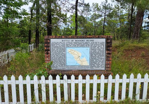 Battle of Roanoke Island Historic Marker about Civil War battle located behind a white picket fence near Manteo, North Carolina.