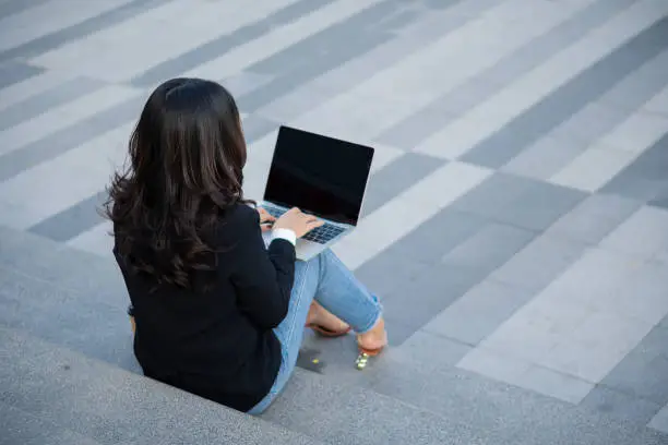 Asian businesswoman with laptop computer working outside looking at screens in the business district, professional women sitting outdoors