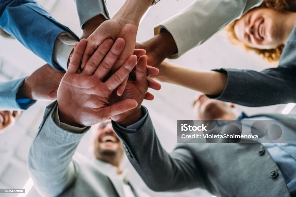 Motivating the team. Shot of multi-ethnic group of business people with stacked hands showing unity and teamwork. Low angle view of successful business people stacking hands in the office. Business Person Stock Photo