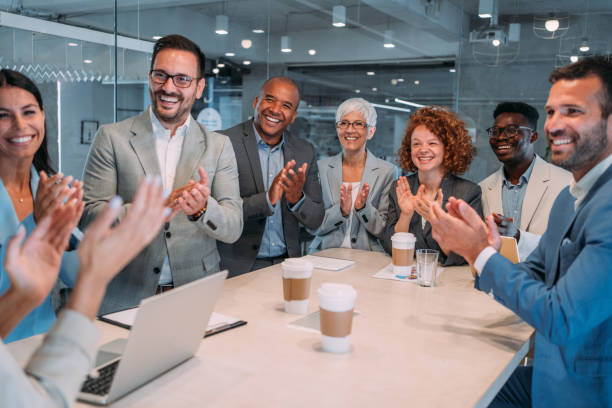 Applauding on a business seminar. Business people clapping hands during business presentation in board room. Group of corporate business persons on a business meeting in modern office. Cheerful team sitting on conference table in board room and clapping with hands after business presentation. Group of happy business people standing in conference hall and applauding. admiration stock pictures, royalty-free photos & images