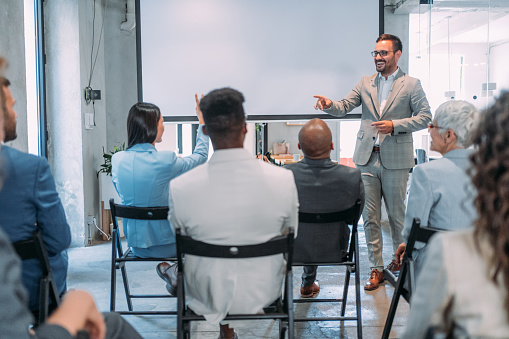 Businessman leading a training class for professionals. Cheerful business leader talking to group of his colleagues on a seminar in conference hall.