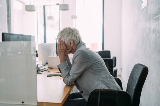 Overworked mature businesswoman in the office. Stressed woman working in modern office. Frustrated businesswoman with head in hands sitting on desk in the office. fired employee stock pictures, royalty-free photos & images