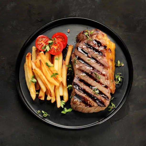 Striploin beef steak with french fries on dark background. Freshly grilled. Healthy dinner. Mediterranean Diet. Top view, flat lay