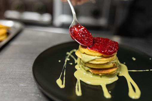 Pancakes with pistachio cream and raspberry jam on a black plate.
