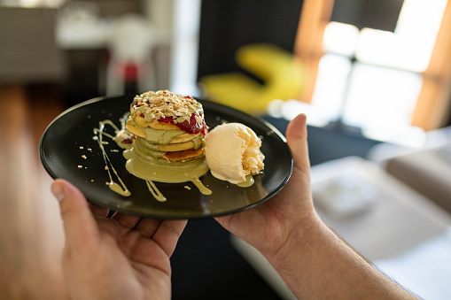 A waiter serves pancakes with ice cream, pistachio cream and raspberry jam