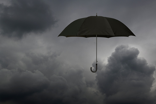 Black umbrella floating in mid-air against storm cloud with copy space.