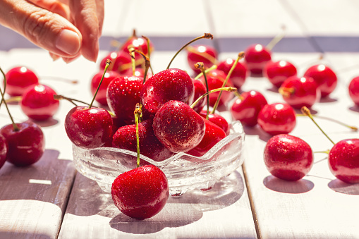 cherries in glass bowl and scattered on white wooden table Red fresh cherry washed, drops shine from sun rays. summer good food on cozy terrace close-up, selective focus. healthy food and diet concept