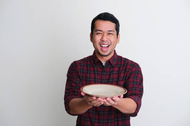 istock Adult Asian man showing enthusiastic expression while holding empty dinner plate 1406140778