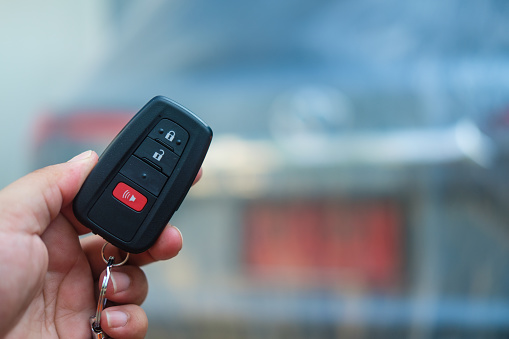 Hand of man holding remote control car key with new modern car background.