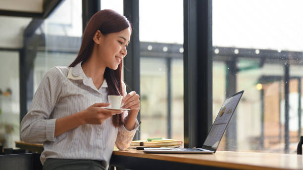 istock Relaxed young employee holding coffee cup and looking at screen of laptop while enjoying work in office. 1406141115