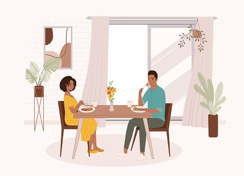 Smiling Black Couple Having Meal Together At The Dining Table Inside Their House. Isolated On Color Background.