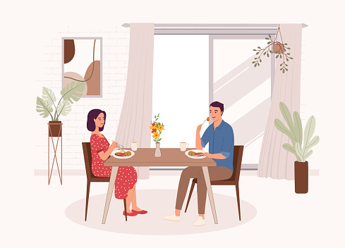 Smiling Couple Having Meal Together At The Dining Table Inside Their House. Isolated On Color Background.