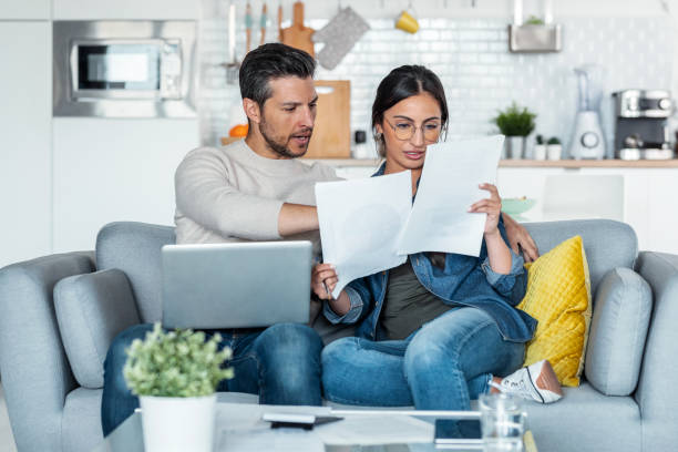 istock Exhausted couple using their laptop to consulting some invoices and documents while sitting on the couch at home. 1406144884