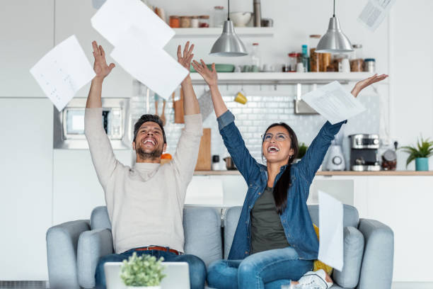 istock Exhausted couple tossing invoices and documents into the air while sitting on the couch at home. 1406145021