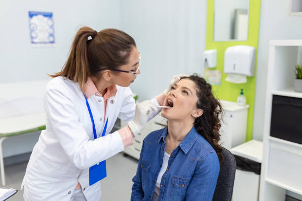 paziente di sesso femminile che apre la bocca affinché il medico le guardi in gola. l'otorinolaringoiatra esamina il mal di gola del paziente. - la bocca apre foto e immagini stock