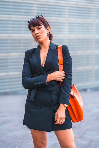 Fashion pose. Brunette girl in the city with a red bag and modern sunglasses looking at the camera