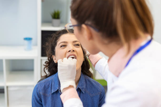 female patient opening her mouth for the doctor to look in her throat. otolaryngologist examines sore throat of patient. - tonsill bildbanksfoton och bilder