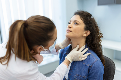 Endocrinologist examining throat of young woman in clinic. Women with thyroid gland test . Endocrinology, hormones and treatment. Inflammation of the sore throat