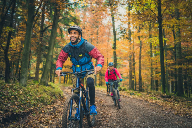Smiling young black man enjoying sport with friends in nature Smiling young adult black man enjoying sport with friends in nature. Adventure trip in colourful autumn forest, active lifestyle concept. cycling stock pictures, royalty-free photos & images