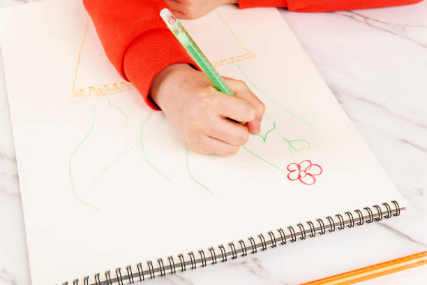 A teenage boy lying on the floor draws a Christmas tree with colored pencils