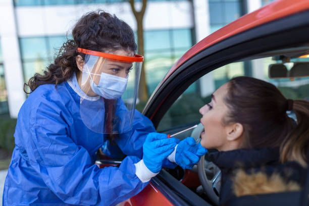istock Medical worker performing drive-thru COVID-19 check,taking nasal swab specimen sample from female patient through car window,PCR diagnostic for Coronavirus presence,doctor in PPE holding test kit 1406153416