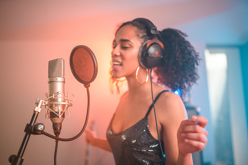 Young Hispanic beautiful female singer singing and recording songs in recording studio. Waist-up, eyes closed.