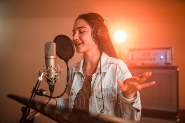 Young charming Asian female singer singing and recording songs in recording studio. Waist-up, eyes closed.