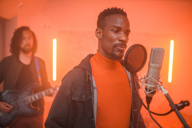 Multi-ethnic music group with Black singer is recording songs in music recording studio. Waist-up shot, all focused and looking away.