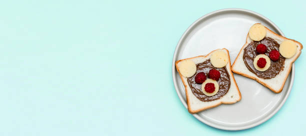 istock Funny bear face sandwich toast bread with peanut butter, cheese and raspberry on plate blue background. Kids child sweet dessert breakfast lunch food close up 1406156467