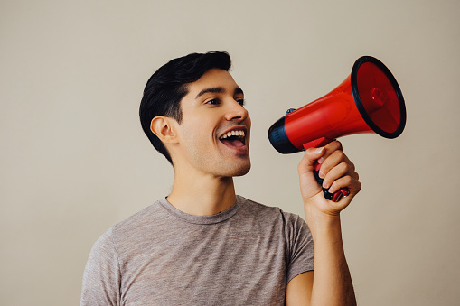 Portrait hispanic latino man holding red megaphone smiling handsome young adult gray t-shirt looking away at copy space studio shot