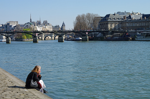 Paris, France - March 21, 2009: A lonely woman sits in thought by the water on the banks of the Seine. Sunny day in March.