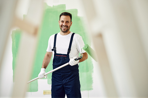 Happy male worker painting the wall in green color and looking at camera.