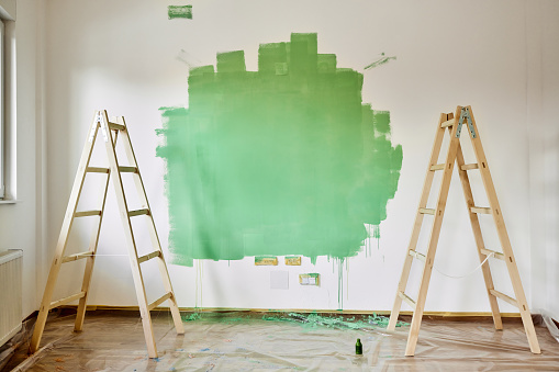 Green paint on the wall and ladders during home renovation process. Copy space.