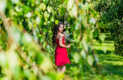 Fancy teen girl in red dress enjoying pure nature on summer day.