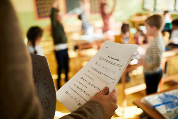 Close up of unrecognizable male teacher holding education exam during music class at elementary school.