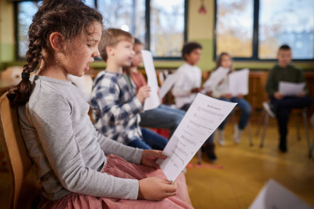Schoolgirl practicing with sheet music on a class at school. Elementary student singing with musical notes on a music class at school. school choir stock pictures, royalty-free photos & images