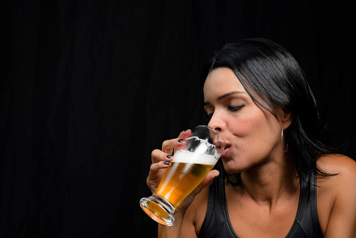 Portrait of a woman with glass of beer against black background. Salvador, Bahia, Brazil.