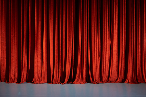 Closed red curtains on stage in theater.