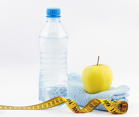 Healthy lifestyle concept. Bottle of water with apple, measuring type  and fitness towel on white background