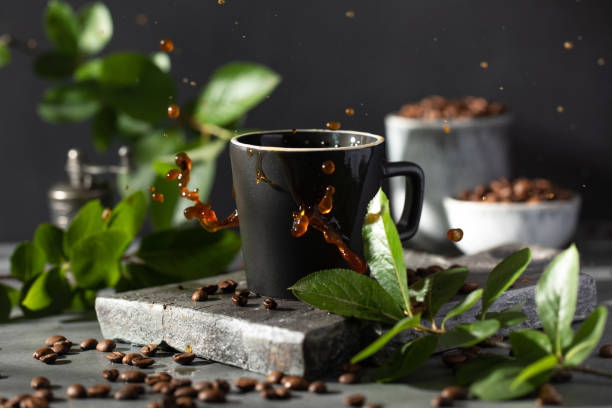 istock Coffee splashes from a coffee mug on a dark background surrounded by roasted coffee beans and branches with green leaves 1406168133