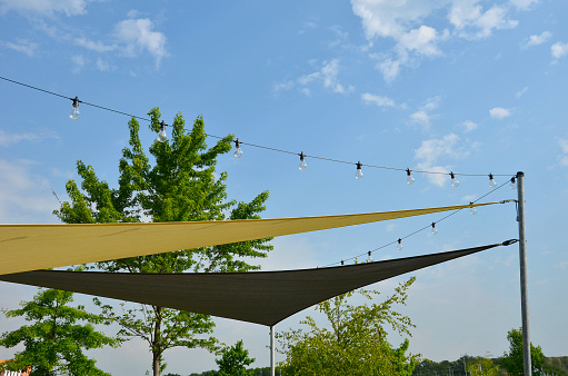 white canvas stretched, shading from sun and rain over terrace ofrestaurant, on playground in kindergarten, on platform of the promenade. pergola with metallic gray beams , cable, electric, bulb, led, shadow, tarp,  lights, light