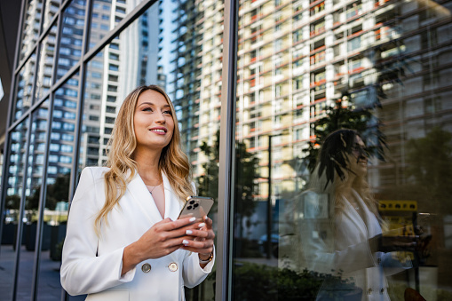 Portrait of female entrepreneur in white blazer holding smart phone. Modern businesswoman.
