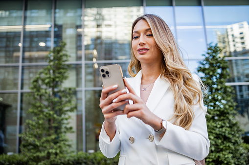Businesswoman coming back from work. Beautiful woman in elegant blazer is using her smart phone. Lifestyle and technology.