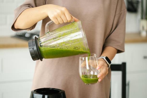 istock Female hands pour green smoothie into a glass close up. 1406173861