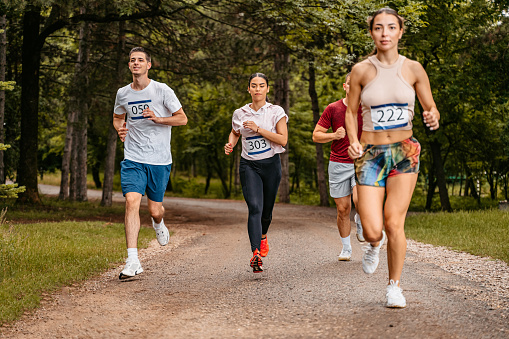 Group of young fit people running a marathon in the park, during the day.