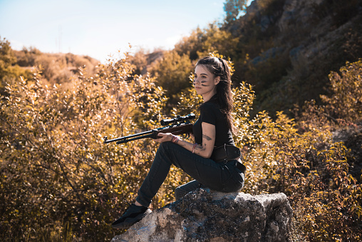 young  female hunter in top with a rifle, in summer at nature. shooter
