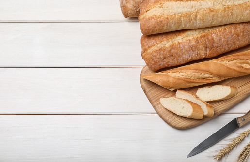 Fresh tasty baguettes, knife and spikelets on wooden table, flat lay. Space for text