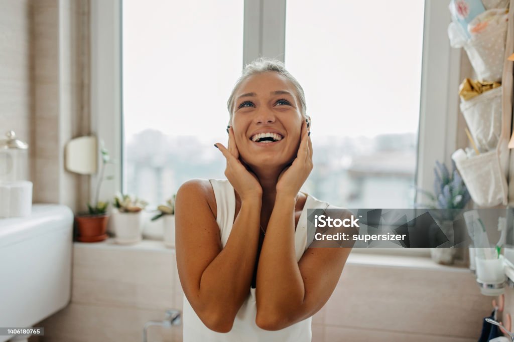 I love my mornings Portrait of young blonde woman holding hands next to her face in the bathroom Mirror - Object Stock Photo